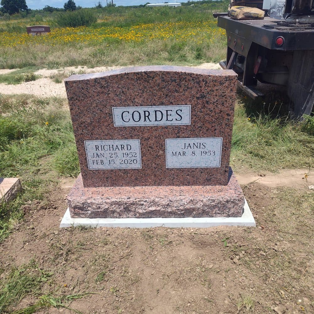 Red granite companion upright monument with a raised polished nameplate, set at a Texas cemetery