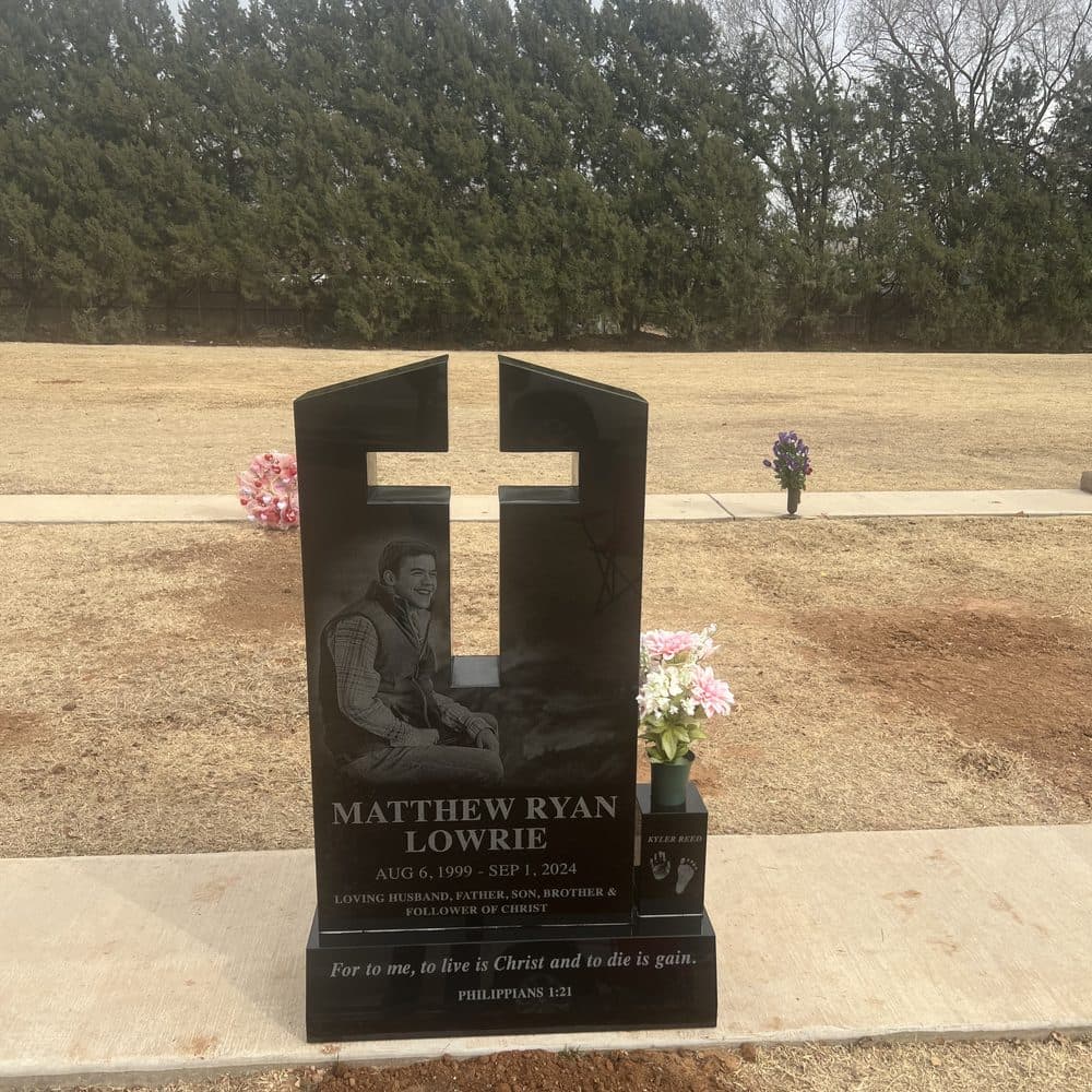 Black granite single upright monument with a raised engraved cross, set at a Texas cemetery