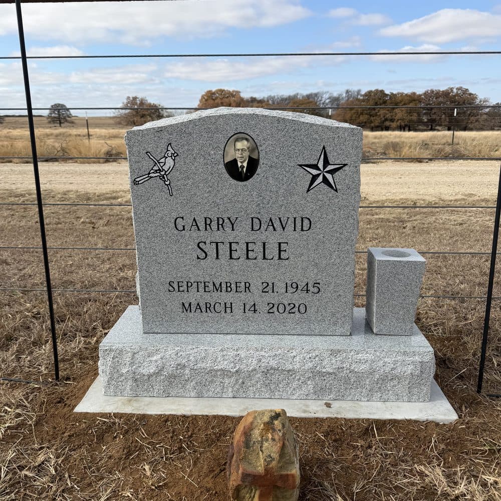 Gray granite single upright monument with an engraved emblem, set at a Texas cemetery