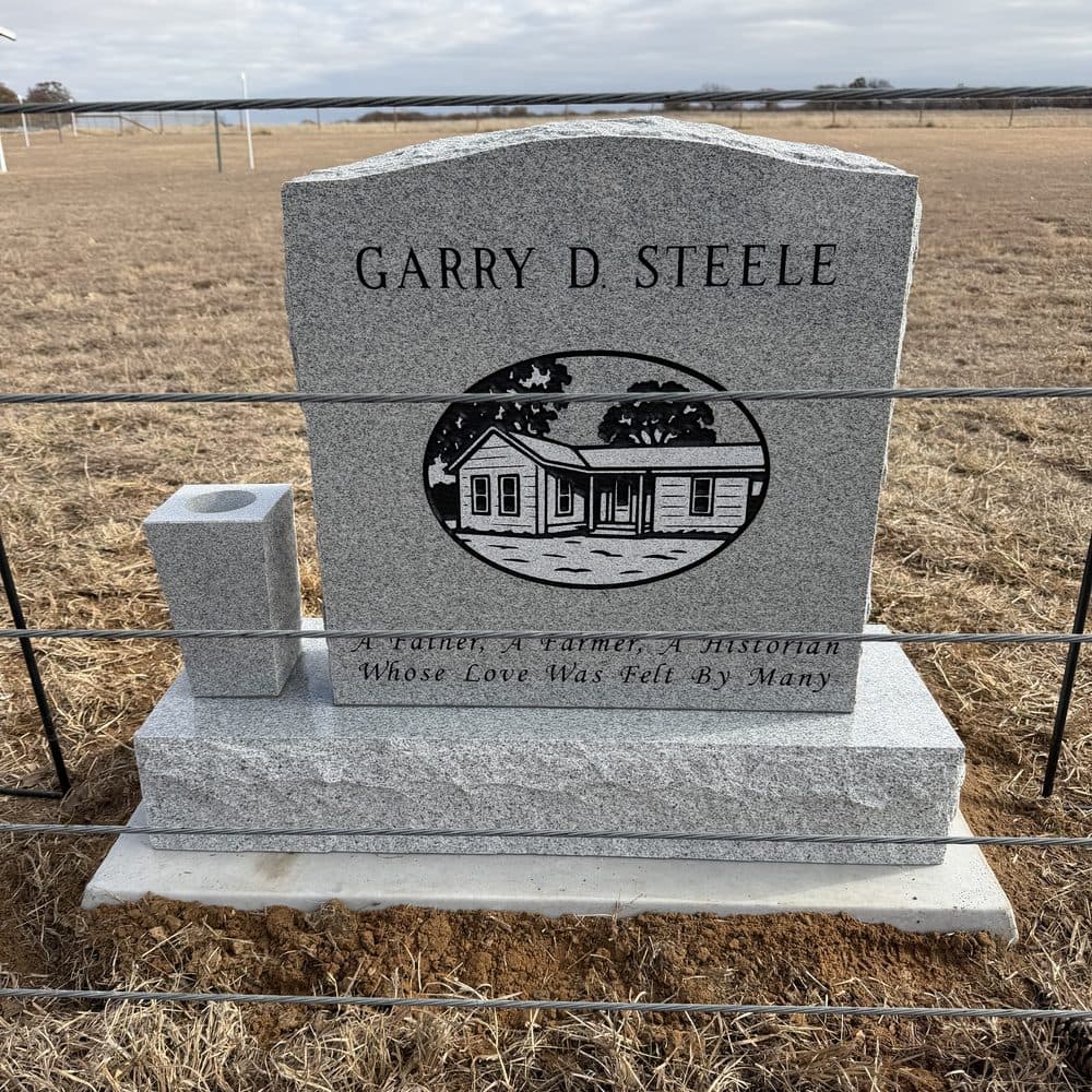 Gray granite single upright monument with an engraved homestead scene, set at a Texas cemetery