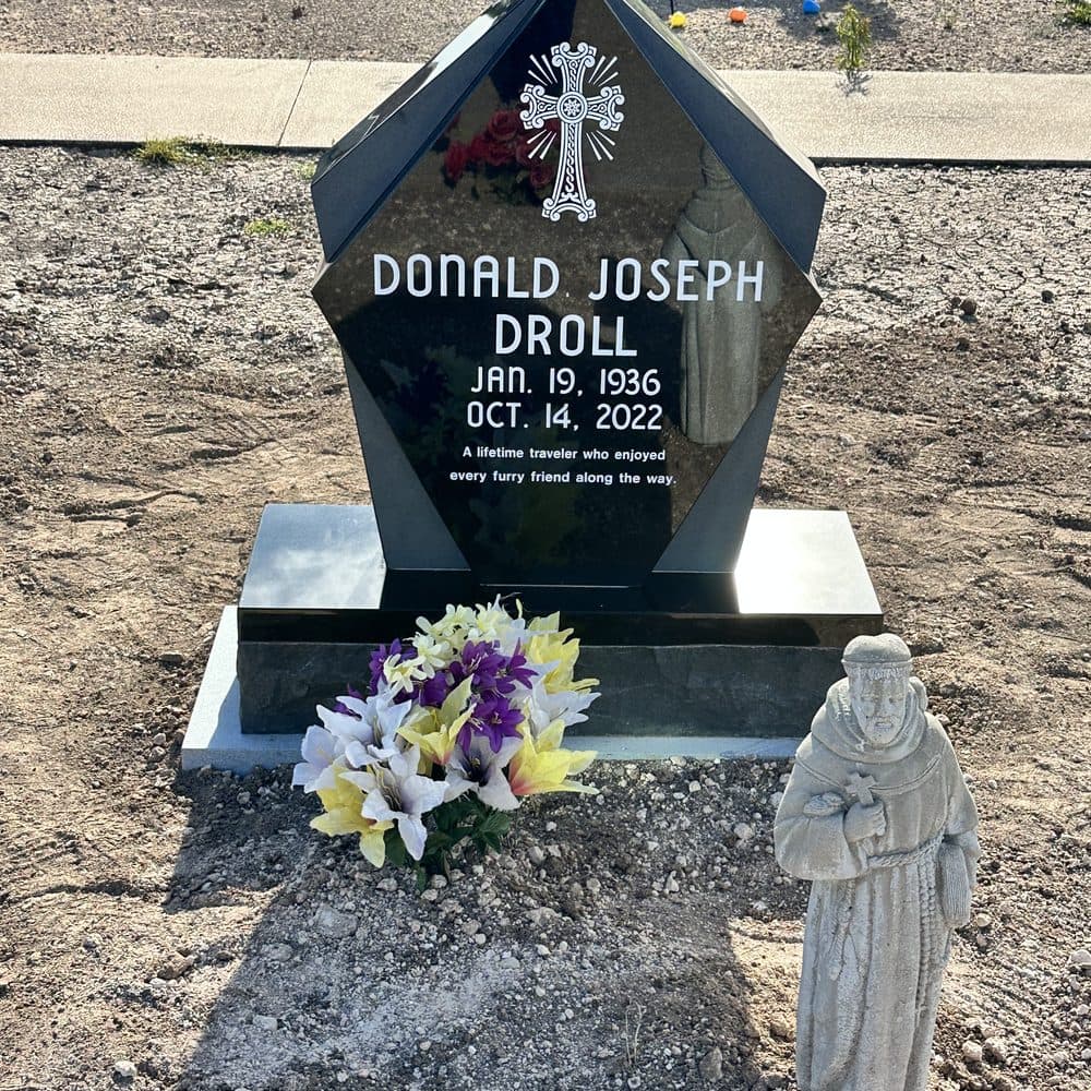 Gray granite single upright monument with an engraved cross, set at a Texas cemetery