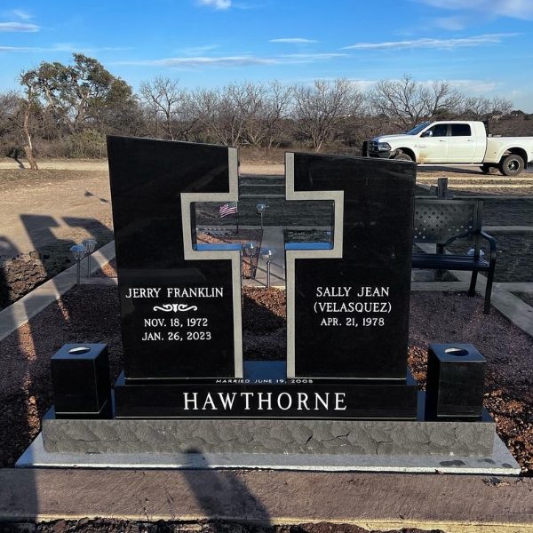 Polished black granite companion headstone with an engraved cross and family name, set at the cemetery